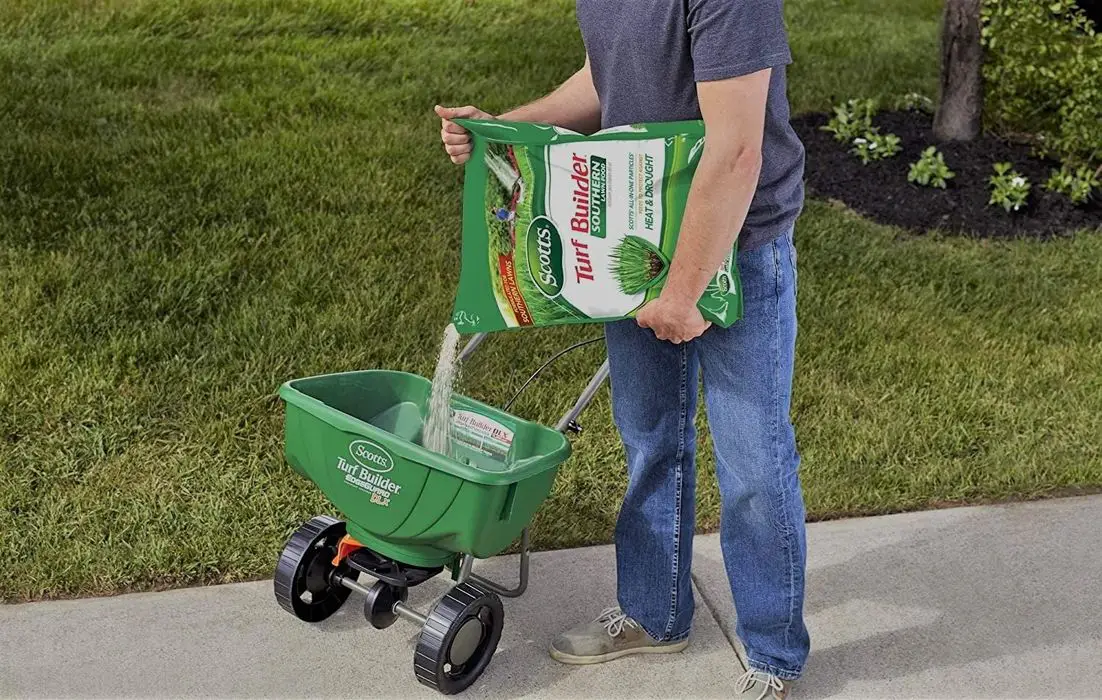 Man pouring Fertilizer for St Augustine Grass into a spreader. The fertilizer brand is Scotts Turf Builder Fertilizer for St Augustine Grass